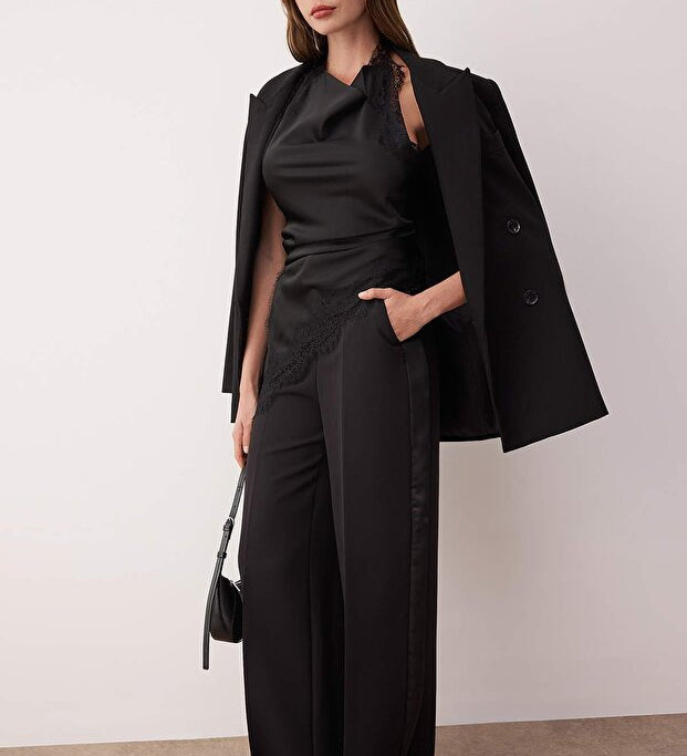 Woman wearing a black outfit with a cape against a plain background