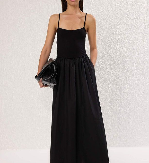 Model in a black sleeveless spaghetti strap maxi dress holding a clutch — elegant and minimal evening outfit for women.”