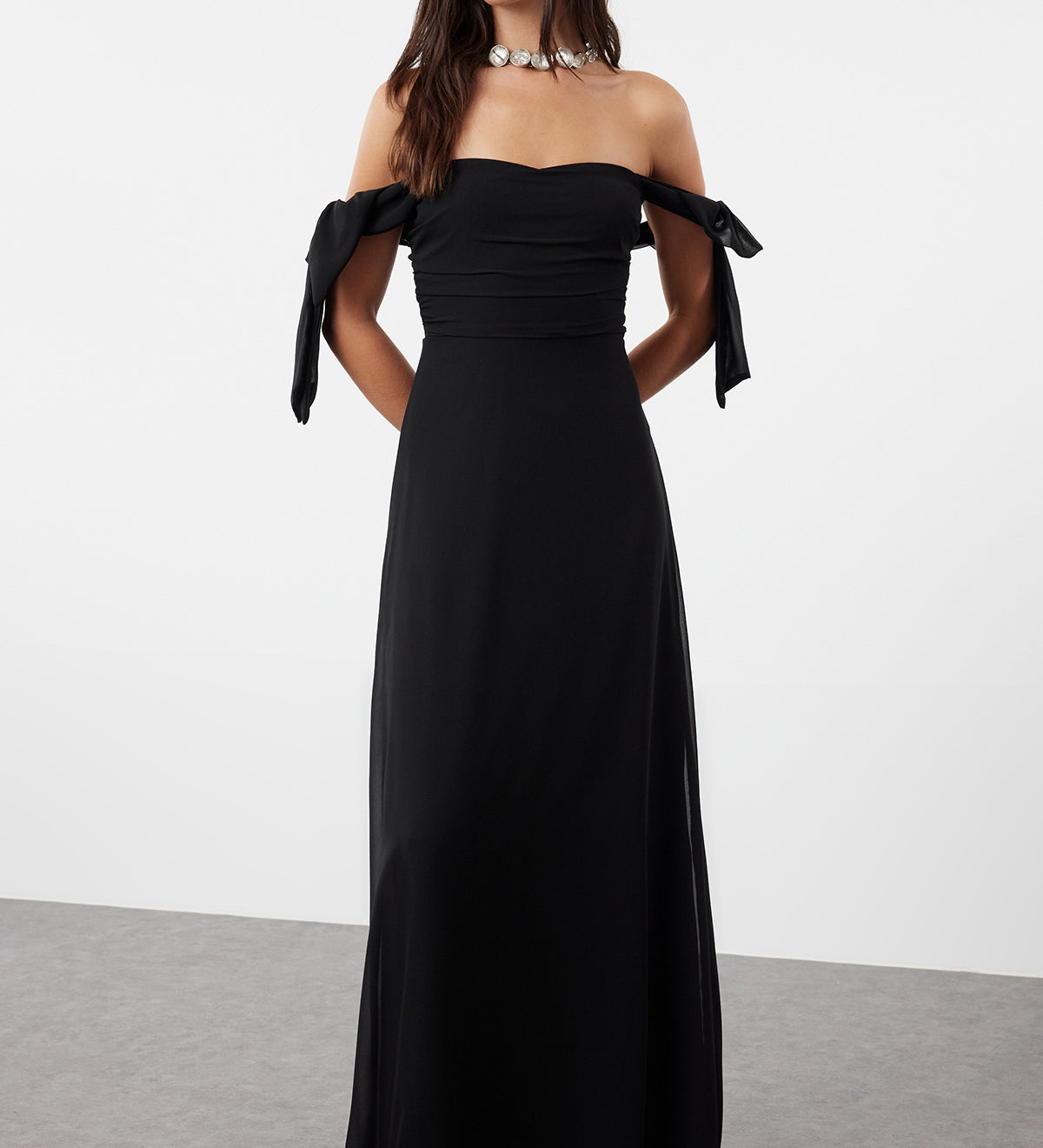  Woman wearing an elegant black off-shoulder maxi dress with tie sleeves and flowing skirt – AtikaStyle.”
