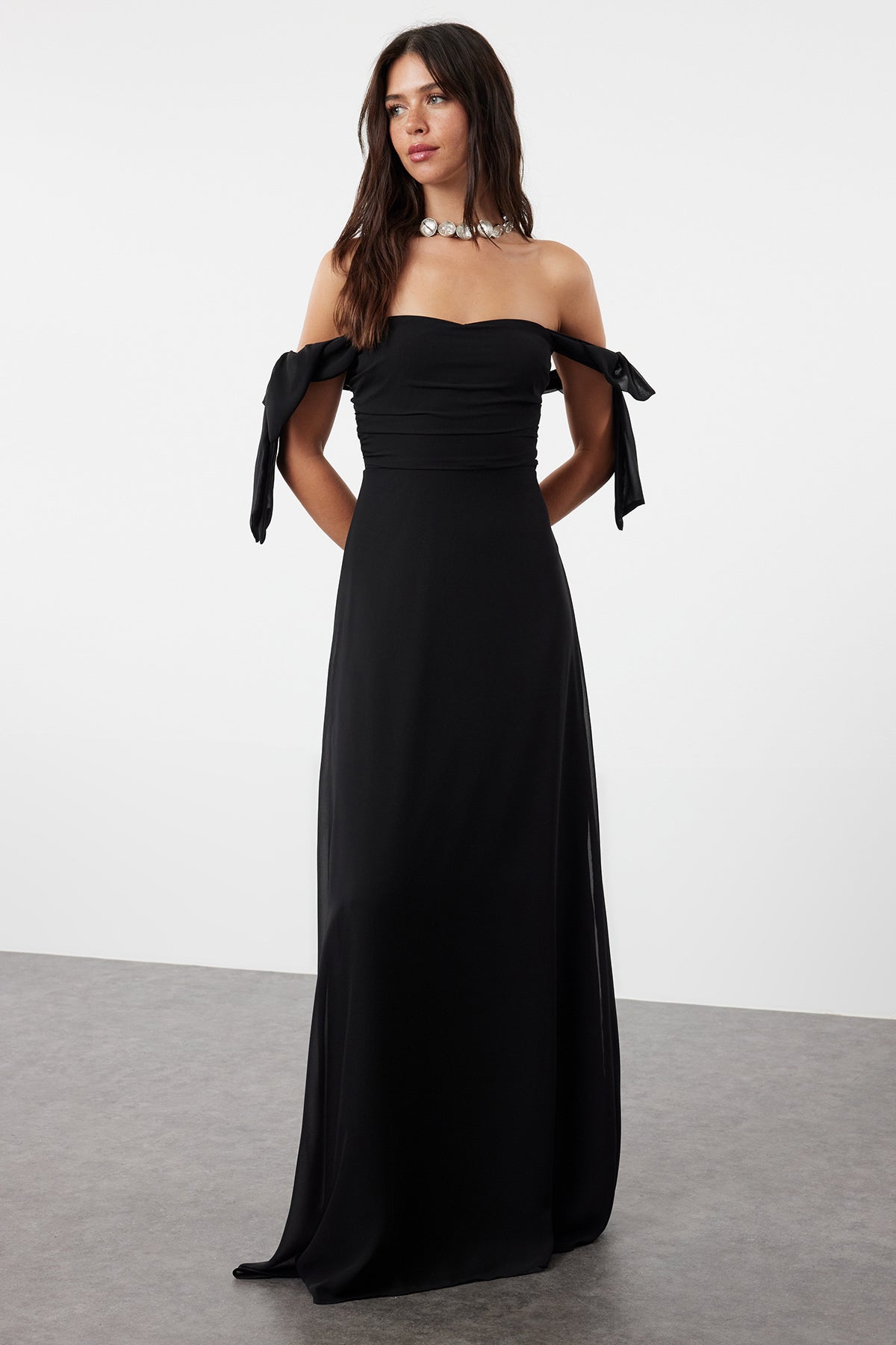  Woman wearing an elegant black off-shoulder maxi dress with tie sleeves and flowing skirt – AtikaStyle.”
