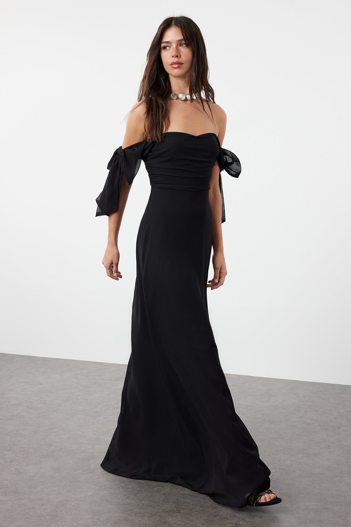  Woman wearing an elegant black off-shoulder maxi dress with tie sleeves and flowing skirt – AtikaStyle.”
