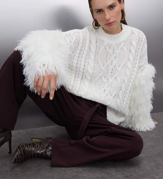 Elevate your look with AtikaStyle’s white cable knit sweater featuring dramatic feather-detailed sleeves. A cozy yet bold statement piece for chic styling.