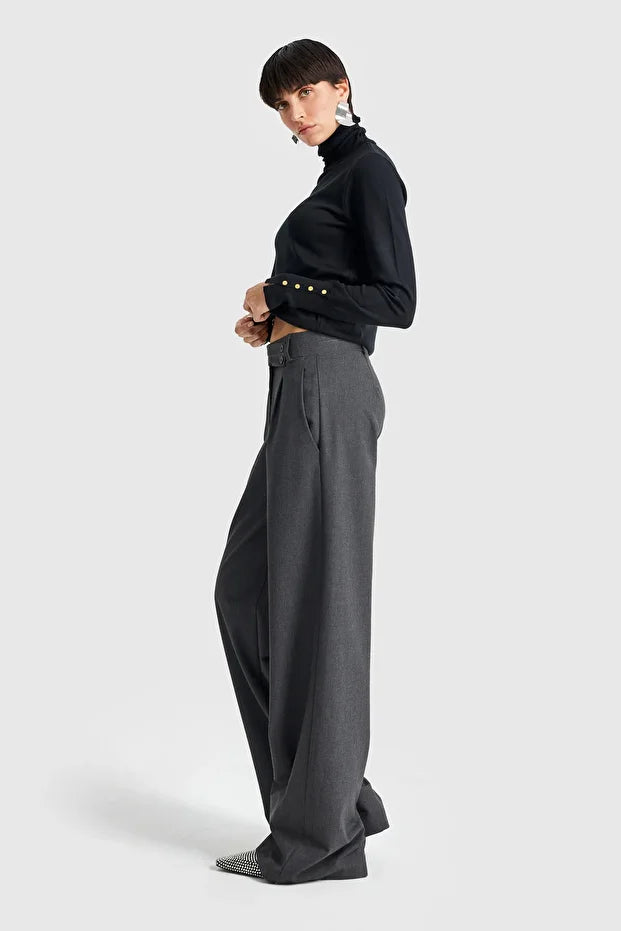 Model wearing charcoal wide-leg tailored trousers styled with a black turtleneck and pointed heels.
