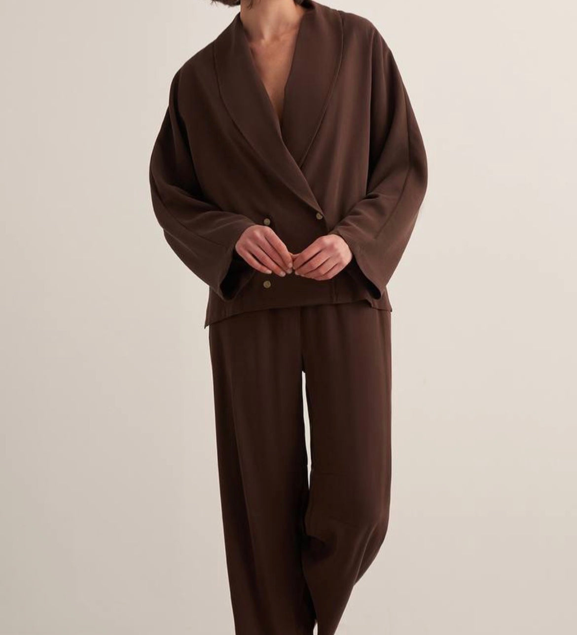 Woman wearing a chocolate brown draped two-piece set with a wrap-style blazer top and wide-leg trousers