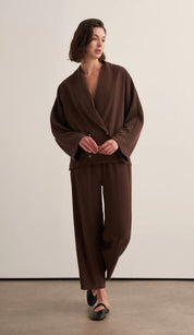 Woman wearing a chocolate brown draped two-piece set with a wrap-style blazer top and wide-leg trousers