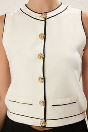 Shop Atikastyle Sleeveless White Knit Vest with Gold Buttons – chic cardigan-inspired top with black piping. A versatile layering piece for work, casual, and evening looks.

