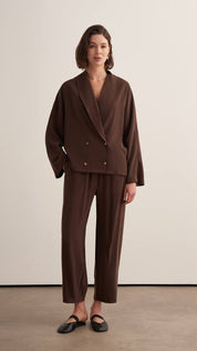 Woman wearing a chocolate brown draped two-piece set with a wrap-style blazer top and wide-leg trousers