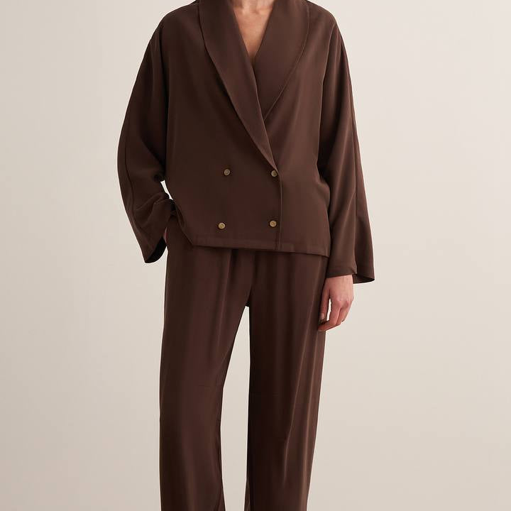 Woman wearing a chocolate brown draped two-piece set with a wrap-style blazer top and wide-leg trousers