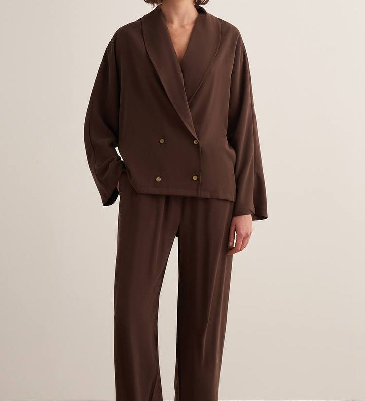 Woman wearing a chocolate brown draped two-piece set with a wrap-style blazer top and wide-leg trousers
