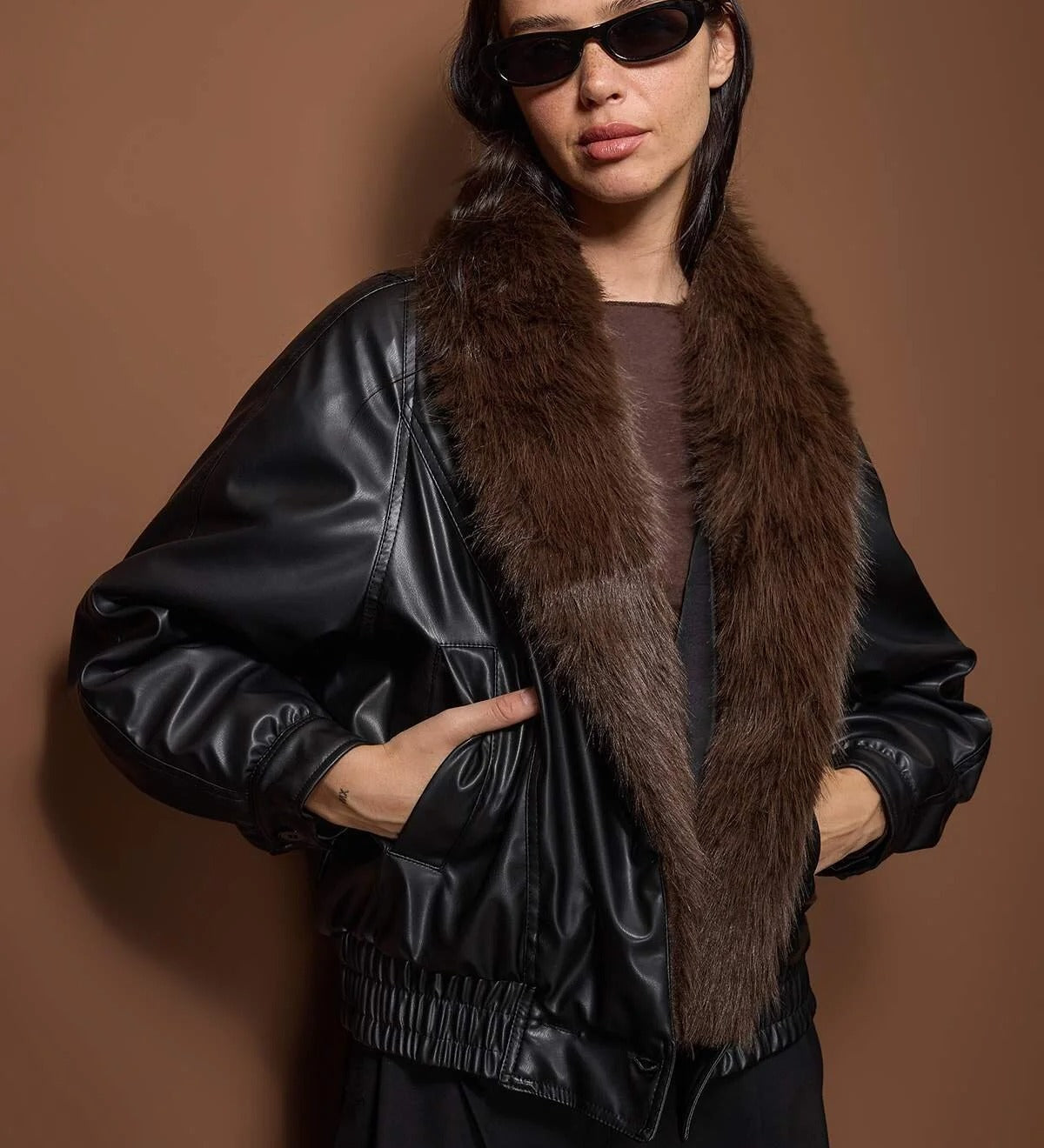 
“Woman wearing a black faux leather bomber jacket with a brown faux fur collar, stylish winter outerwear – AtikaStyle.”
