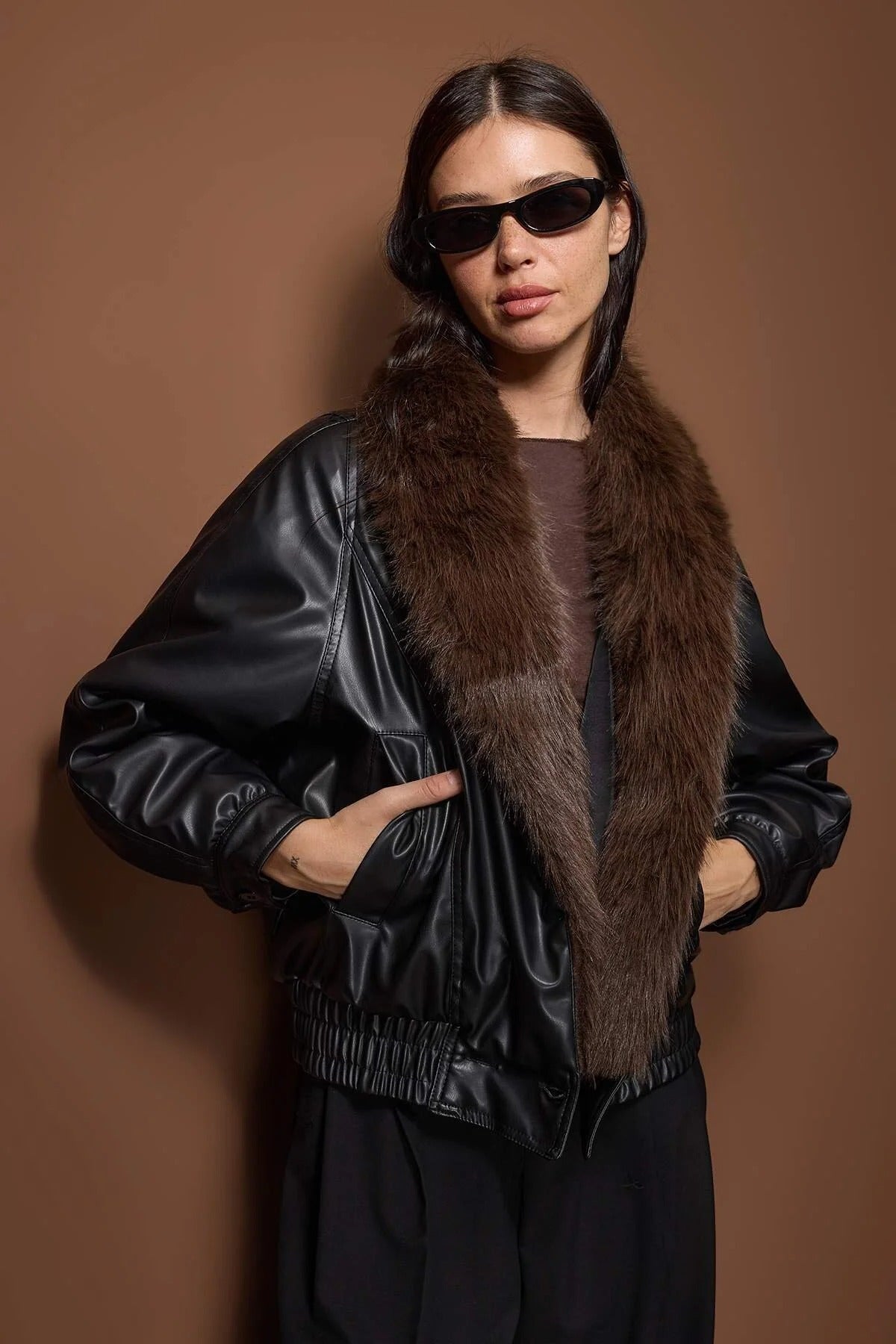 
“Woman wearing a black faux leather bomber jacket with a brown faux fur collar, stylish winter outerwear – AtikaStyle.”
