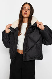 Woman wearing a black puffer jacket with a white interior on a plain background