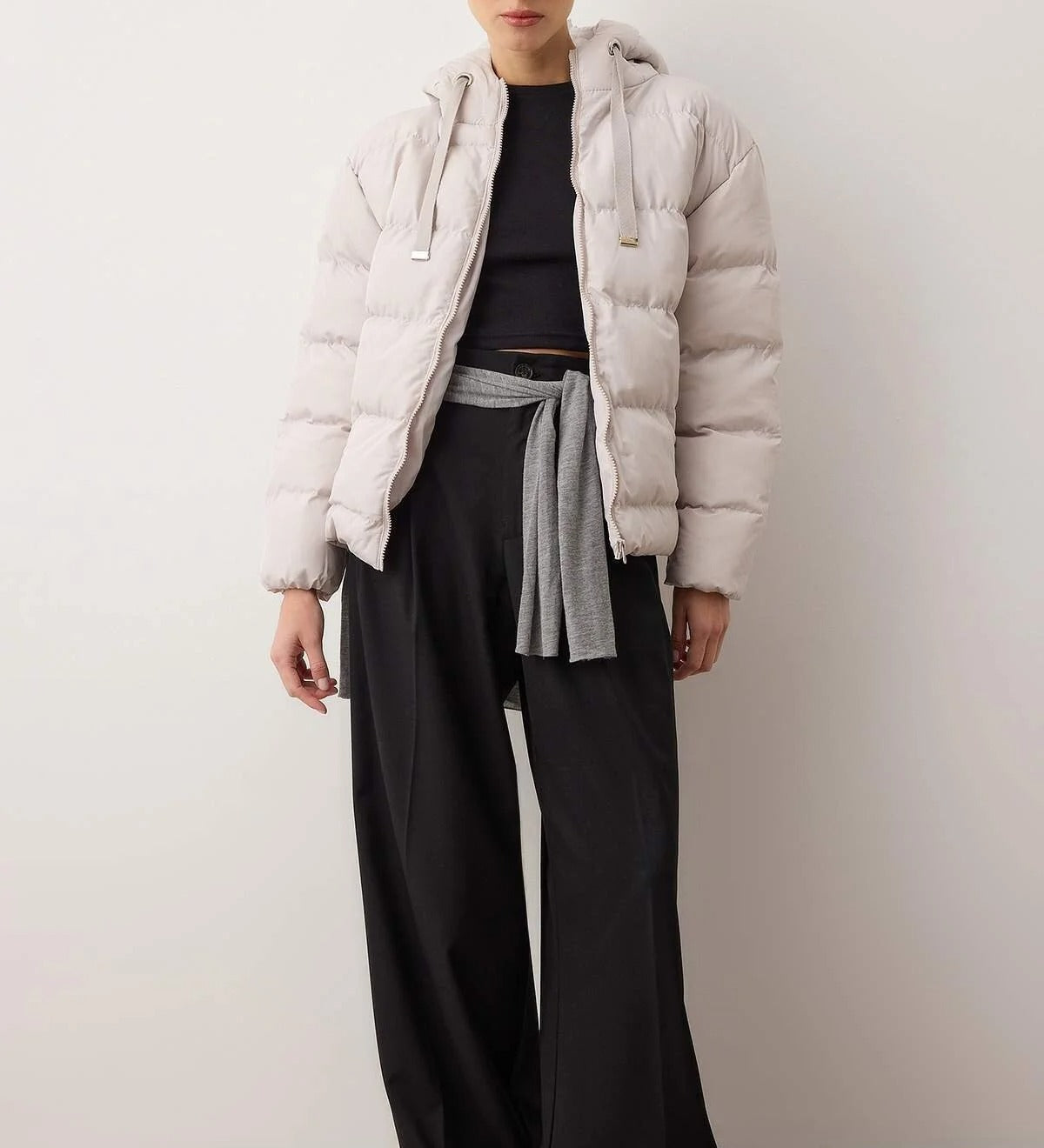 Person wearing a light gray puffer jacket, black top, and wide-leg pants against a white background