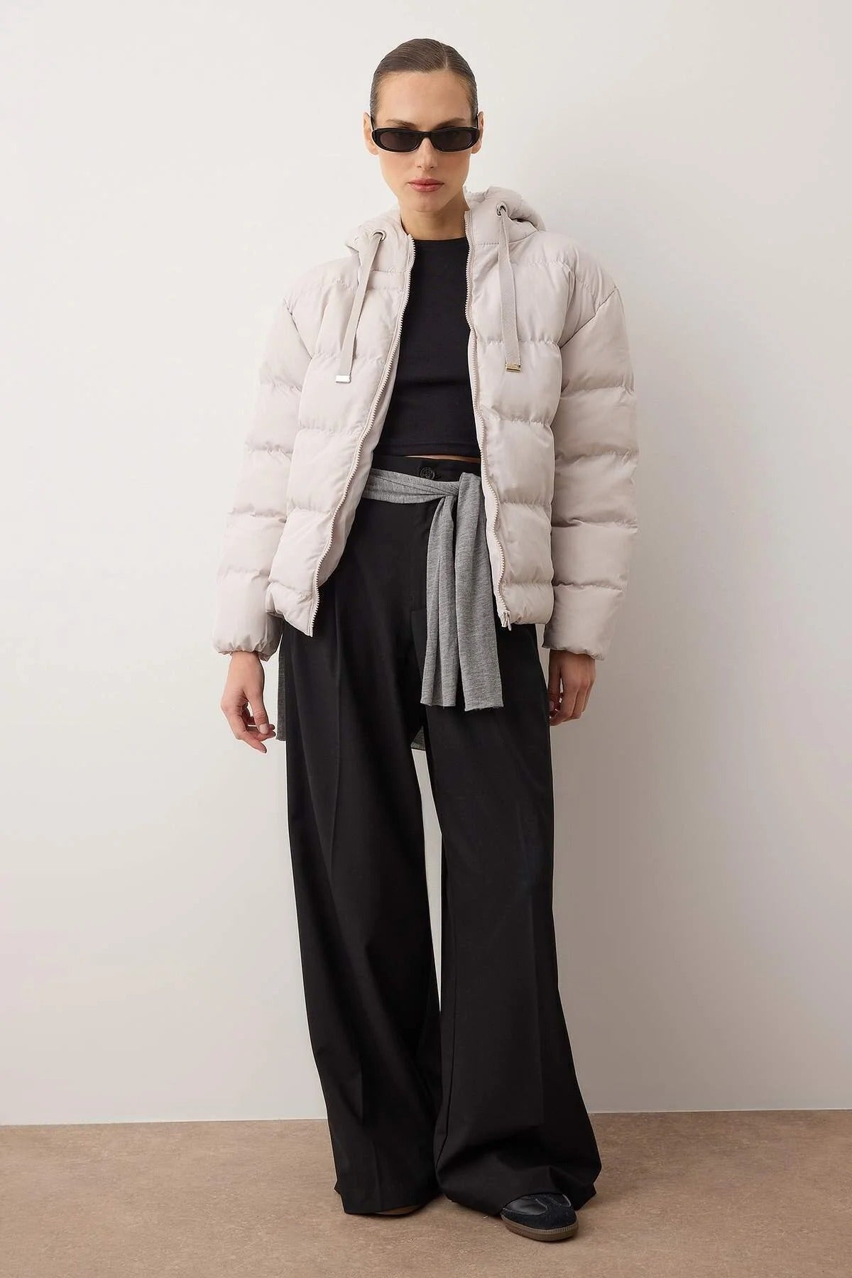 Person wearing a light gray puffer jacket, black top, and wide-leg pants against a white background