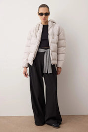 Person wearing a light gray puffer jacket, black top, and wide-leg pants against a white background