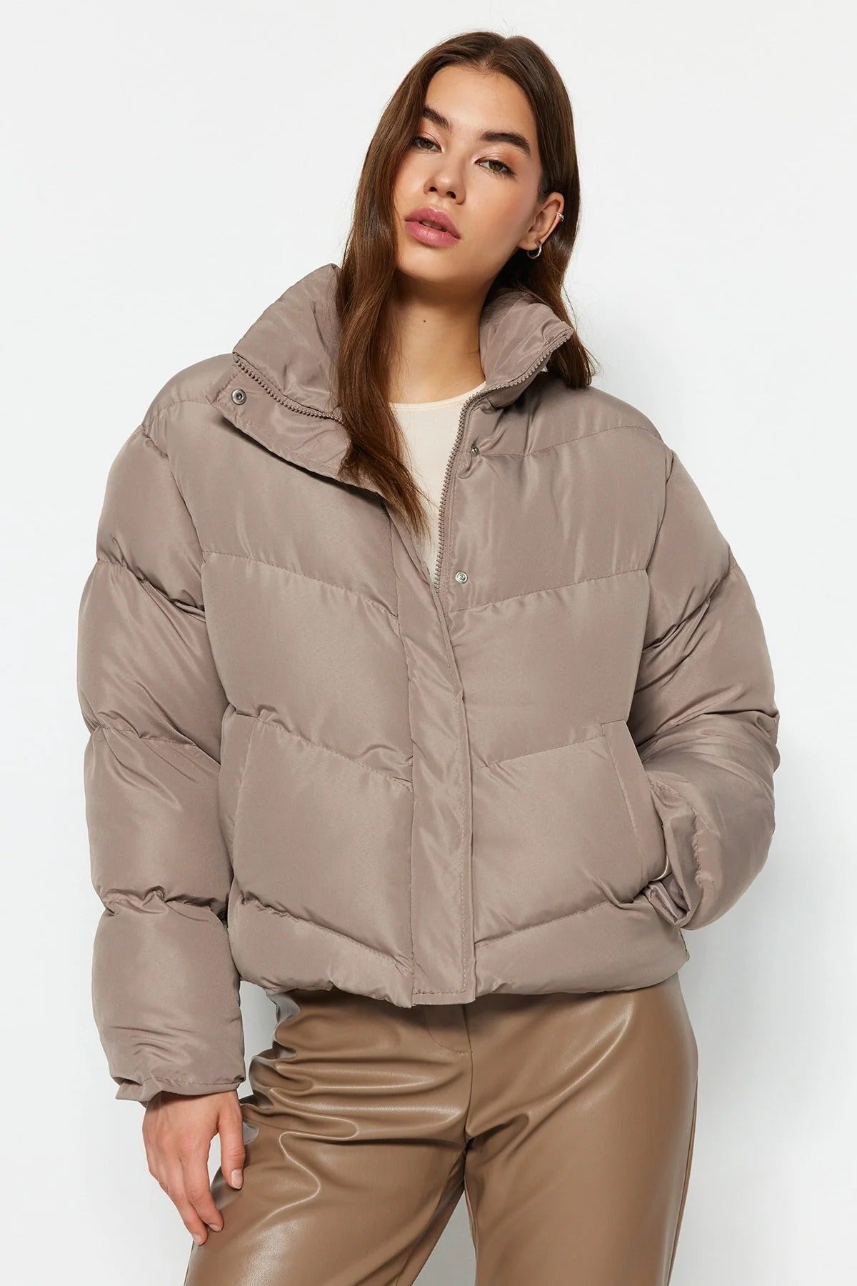 Woman wearing a beige puffer jacket and pants on a white background