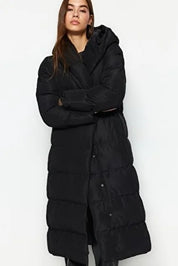 Woman wearing a long black puffer coat against a white background