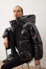 Person wearing a black puffer jacket sitting on a chair against a white background