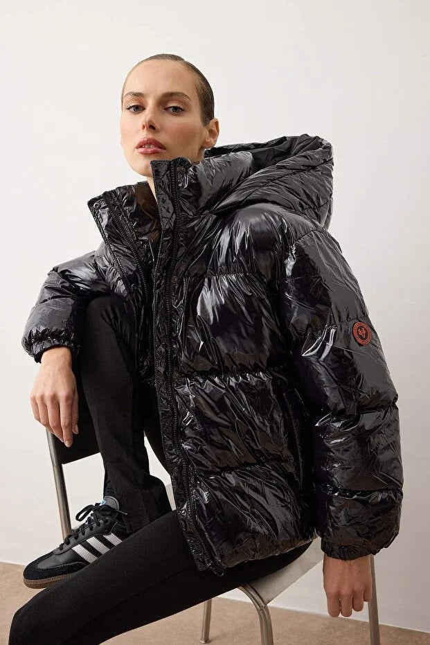 Person wearing a black puffer jacket sitting on a chair against a white background