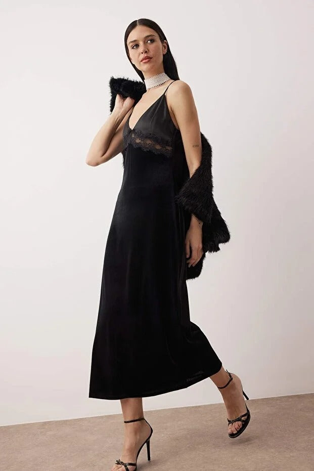 Woman wearing a black dress with sheer details and fur accents against a plain background