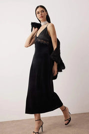 Woman wearing a black dress with sheer details and fur accents against a plain background