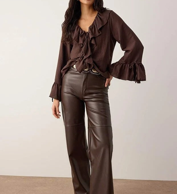 Woman wearing a chocolate brown ruffle blouse with tie-front neckline, paired with brown faux-leather pants — AtikaStyle.”
