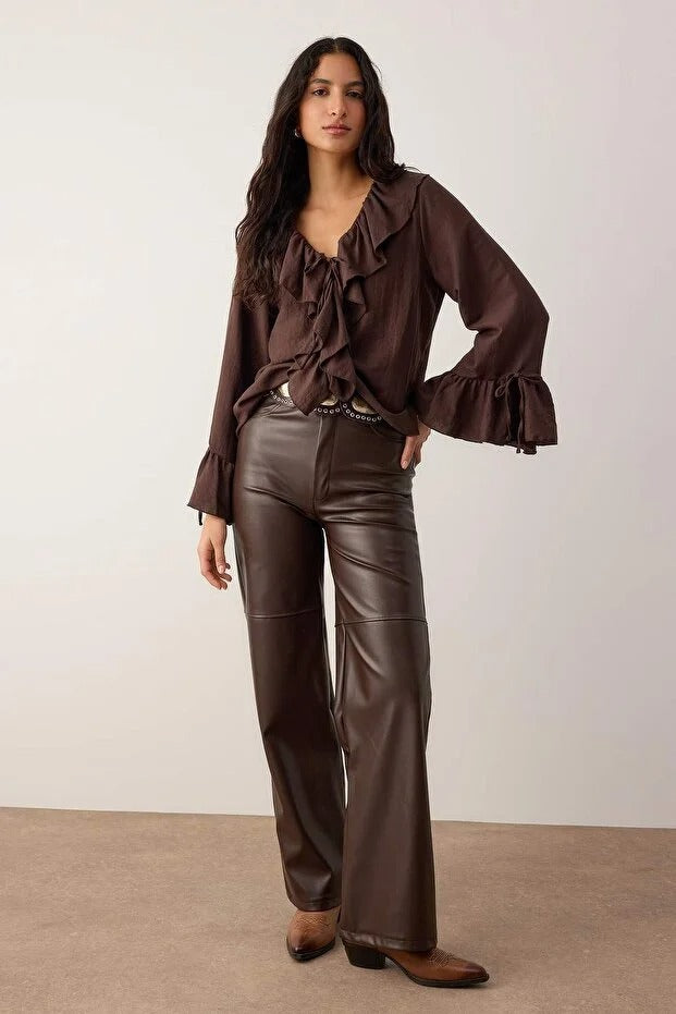 Woman wearing a chocolate brown ruffle blouse with tie-front neckline, paired with brown faux-leather pants — AtikaStyle.”
