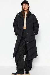 Person wearing a long black puffer coat on a white background