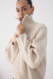 Woman wearing a beige knitted sweater against a white background