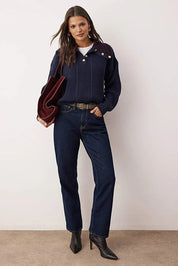 Woman wearing a navy sweater, jeans, and black boots against a white background