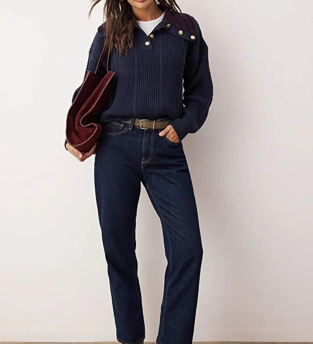 Woman wearing a navy sweater, jeans, and black boots against a white background