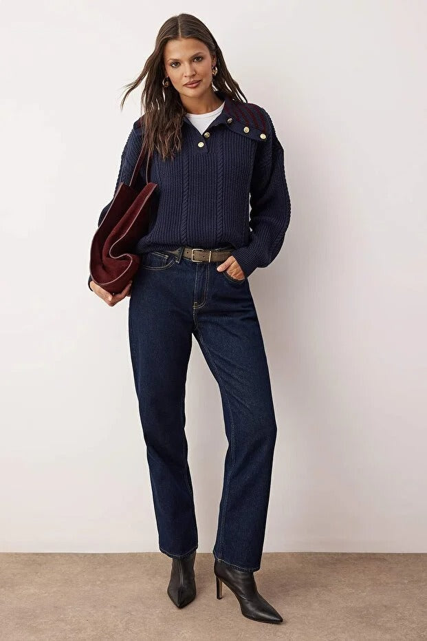 Woman wearing a navy sweater, jeans, and black boots against a white background
