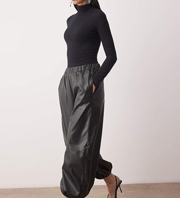Woman wearing a black turtleneck and gray pants on a white background