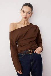 Woman wearing a brown off-shoulder top and blue jeans against a white background