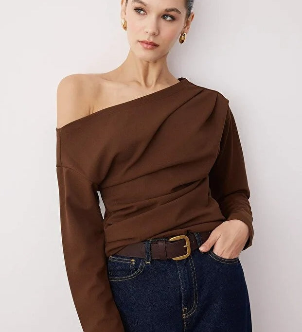 Woman wearing a brown off-shoulder top and blue jeans against a white background