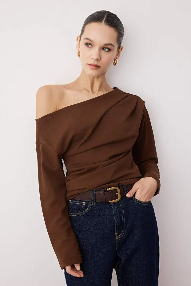 Woman wearing a brown off-shoulder top and blue jeans against a white background
