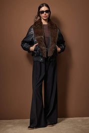 
Woman wearing a black faux leather bomber jacket with a brown faux fur collar, stylish winter outerwear – AtikaStyle.
