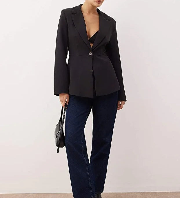 Woman wearing a black blazer and blue pants against a white background