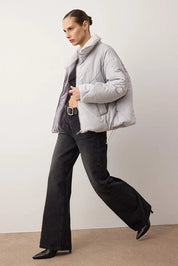 Woman wearing a light gray puffer jacket and black pants against a plain background