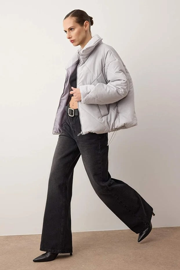 Woman wearing a light gray puffer jacket and black pants against a plain background