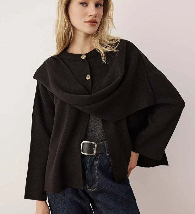 Woman wearing a black poncho over a gray top and blue jeans on a plain background