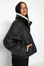 Woman wearing a black puffer jacket with white fur lining on a white background