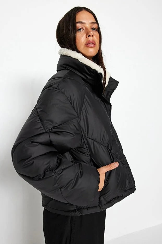 Woman wearing a black puffer jacket with white fur lining on a white background