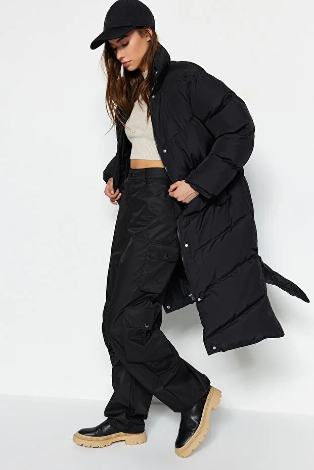 Person wearing a long black puffer coat on a white background