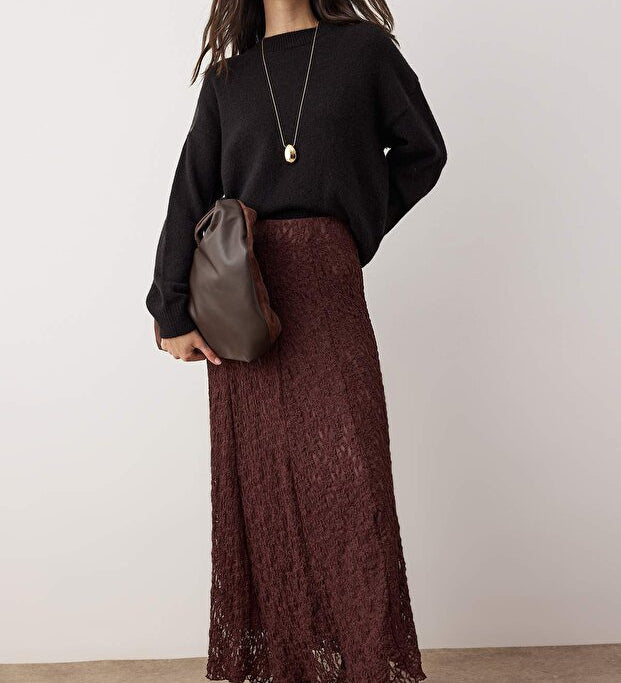 Woman wearing a black sweater and brown lace skirt holding a brown bag against a white background