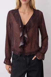 Woman wearing a sheer brown blouse with ruffled details on a plain background