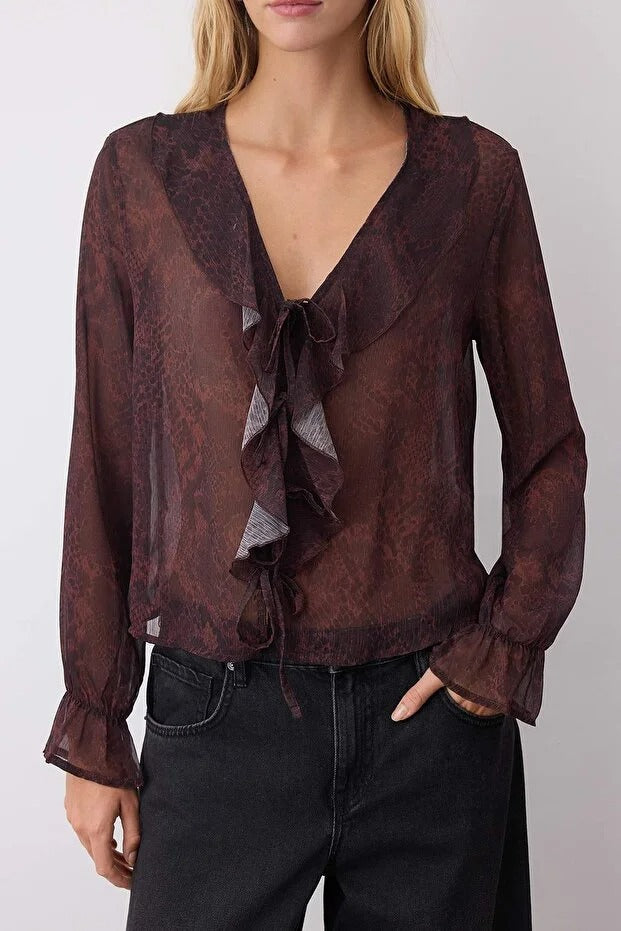 Woman wearing a sheer brown blouse with ruffled details on a plain background