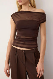 Woman wearing a brown off-shoulder top and pants against a plain background