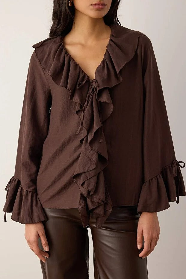 Brown ruffled blouse worn by a model on a plain background