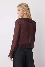 Woman wearing a sheer burgundy top with long sleeves against a white background